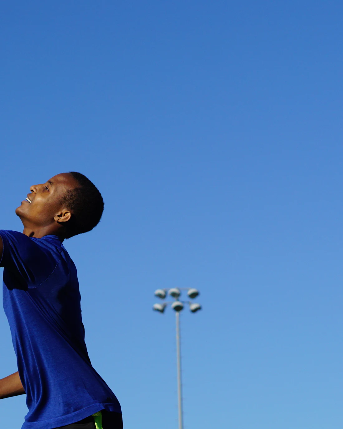 Young athlete in a blue jersey reaching up under a clear sky